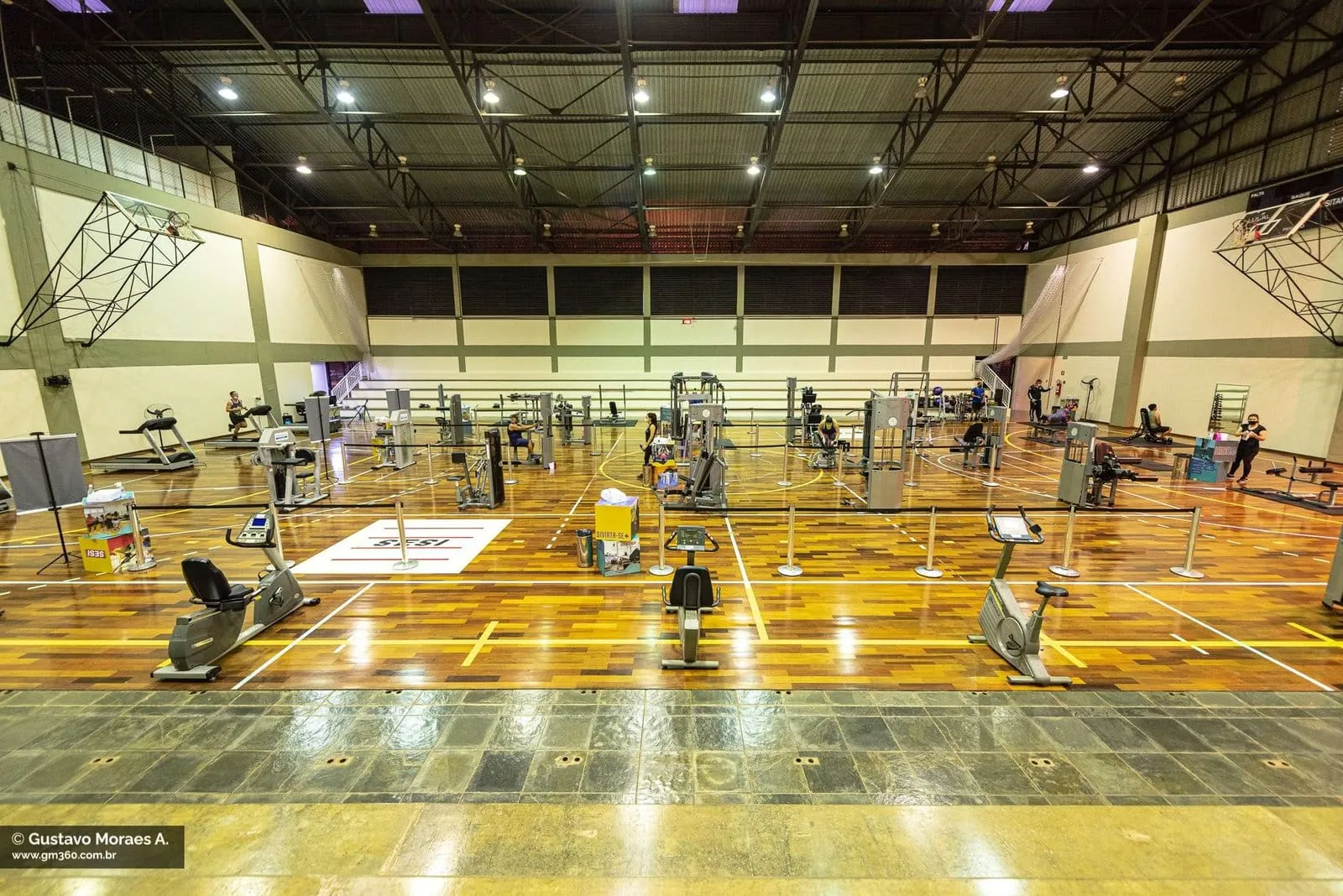 Academia em ginásio com piso de madeira e aparelhos de musculação