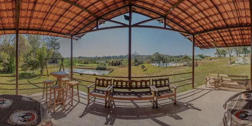 Varanda coberta do Sítio Santa Maria com bancos de madeira e vista para o gramado e o lago